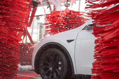 White Tesla sedan between red car wash brushes in Tommy's Express Car Wash 